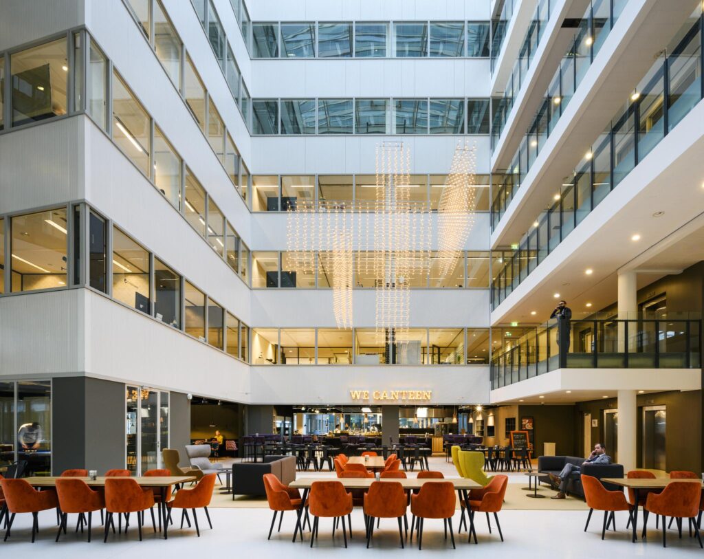 Moderne kantoorlobby aan de Thomas R. Malthusstraat met zithoeken, eetruimte en opvallende verlichtingsinstallatie.